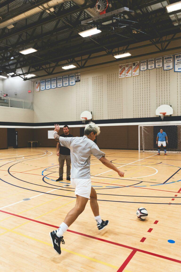 Sporthallen und Spielfeldmarkierungen sind zu sehen und ein Mann der in einer HAlle Fußball spielt