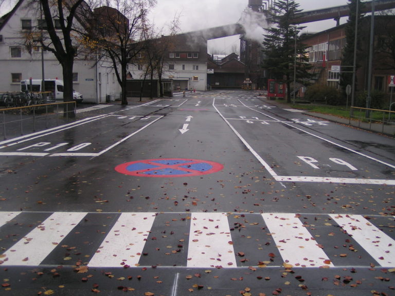 eine Straße mit Zebrastreifen und einer Fabrik, aus der Rauch aufsteigt