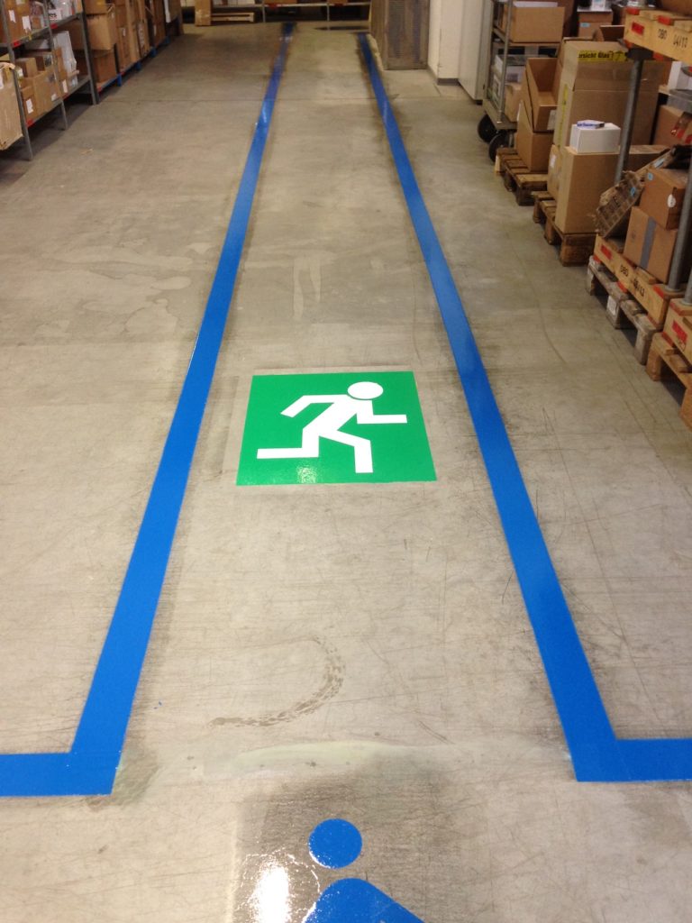Rettungswegmarkierungen zeigen ein grünes und weißes Schild auf einem Betonboden mit blauem Klebeband