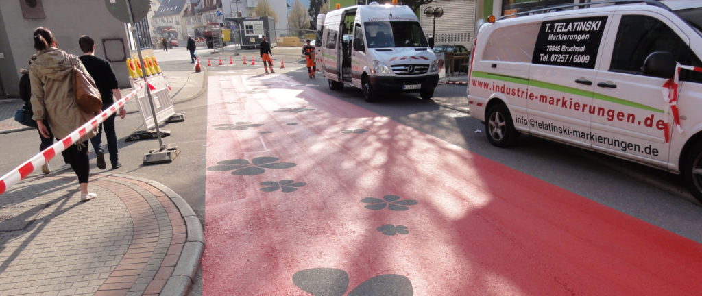 eine rot markierte Straße mit Absperrungen und weißen Lieferwagen