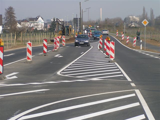 eine Straße mit weißen Straßenmarkierungen, Verkehrskegeln und Autos