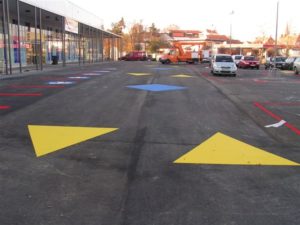 Gelbe Dreiecke und blaue Vierecke die auf dem Boden eines Parkplatzes markiert sind
